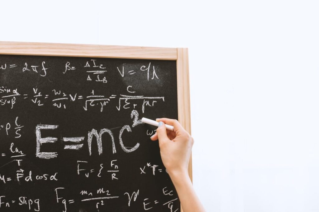 Close-up of hand writing physics equations on a chalkboard indoors.